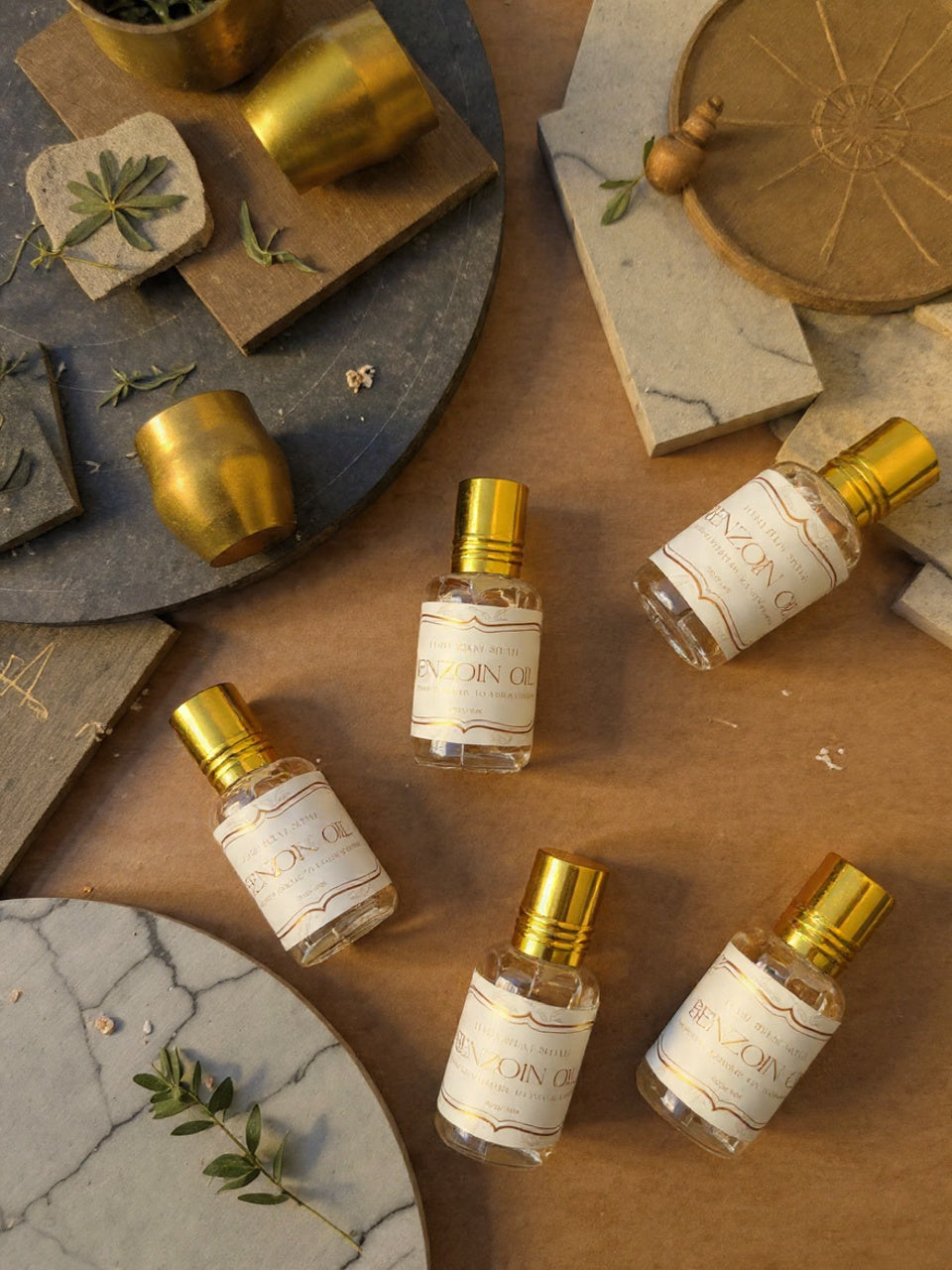 Five small perfume bottles with gold caps on a textured surface with decorative elements.