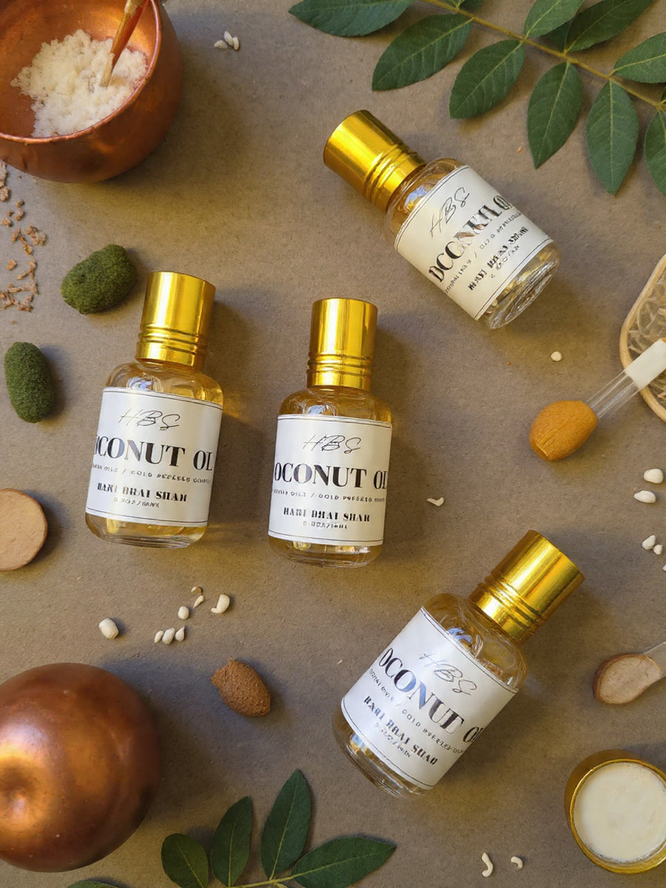 Bottle of coconut oil with gold caps on a textured surface with lcoconut powder and seeds.