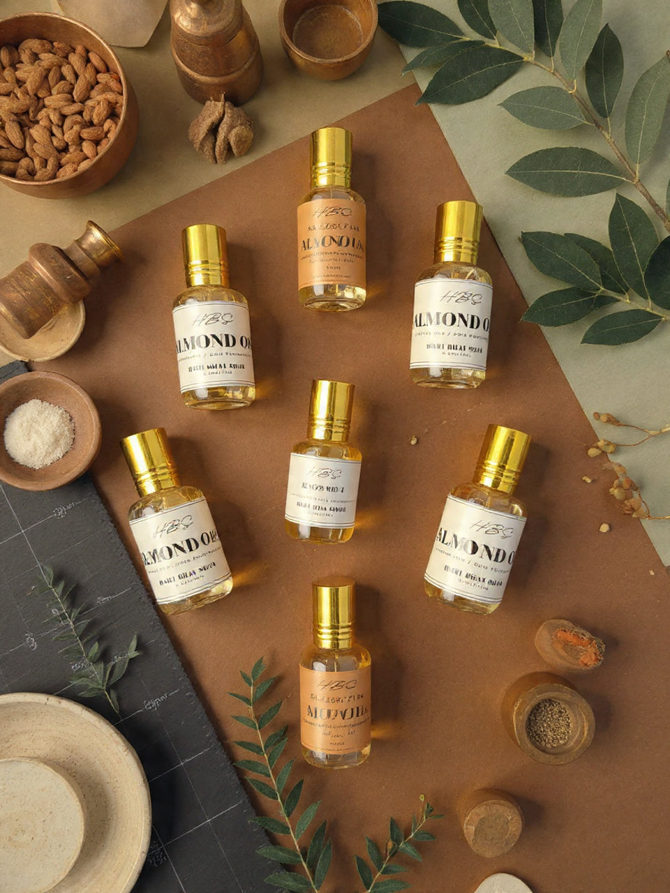 Almond oil bottles with gold caps on a brown surface with almond and leaves.
