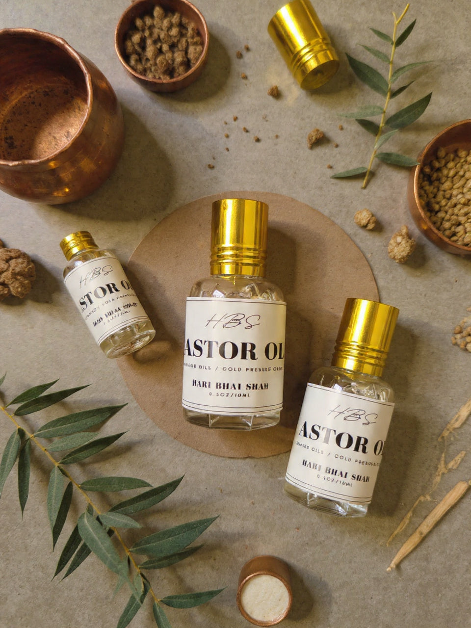 Castor Oil bottles with gold caps on a textured surface with leaves and small containers.