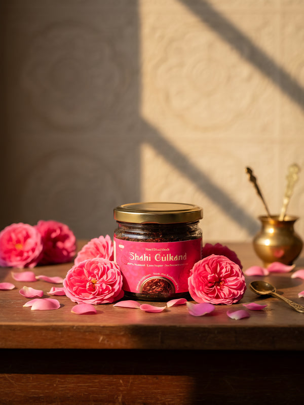 Jar of Shahi Gulaband with pink flowers and rose petals on a wooden surface